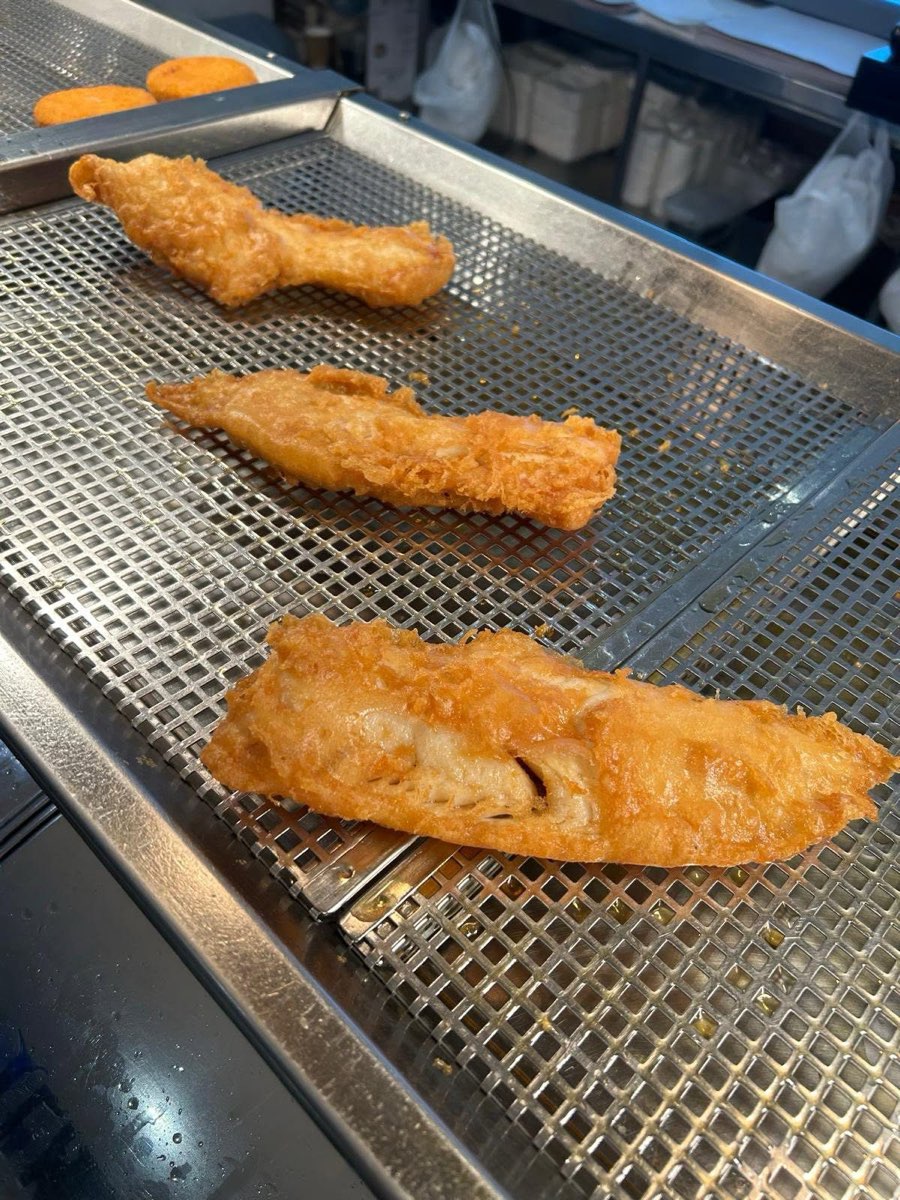 Battered cod resting on the rack above the fryer